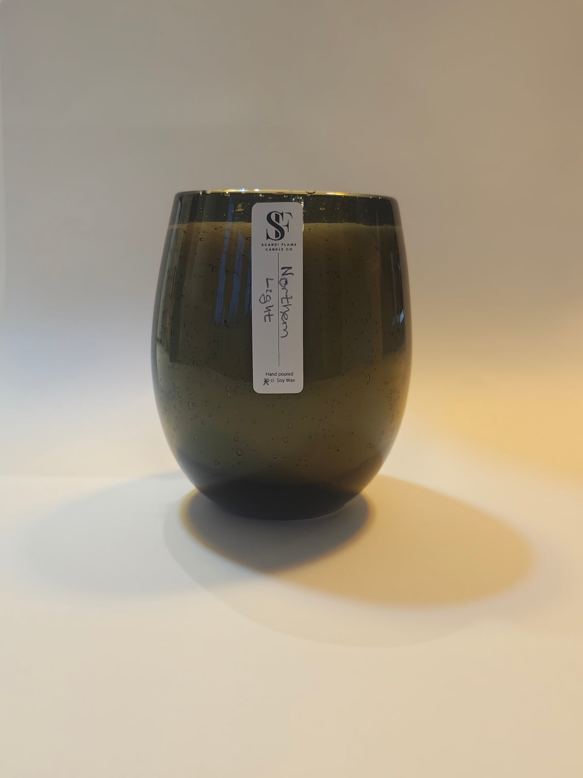 A small ceramic candle jar with a rounded, tulip-like shape, featuring little bubbles in a black see-through glass. A white paper label with a black 'SF' logo is attached to the side.