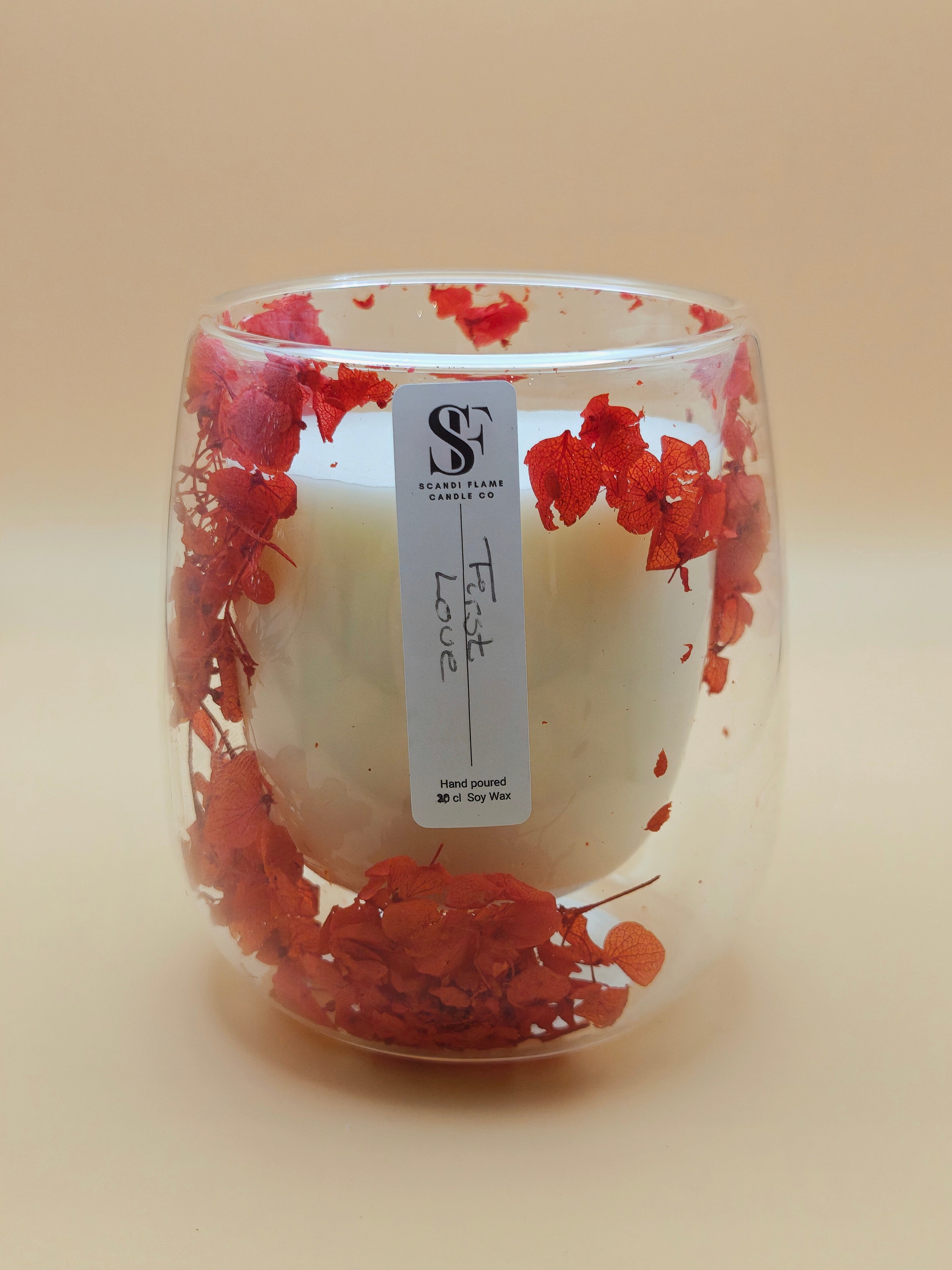 Clear glass jar with red dry flowers in the walls of the jar with 'First Love' label from Scandi Flame.
