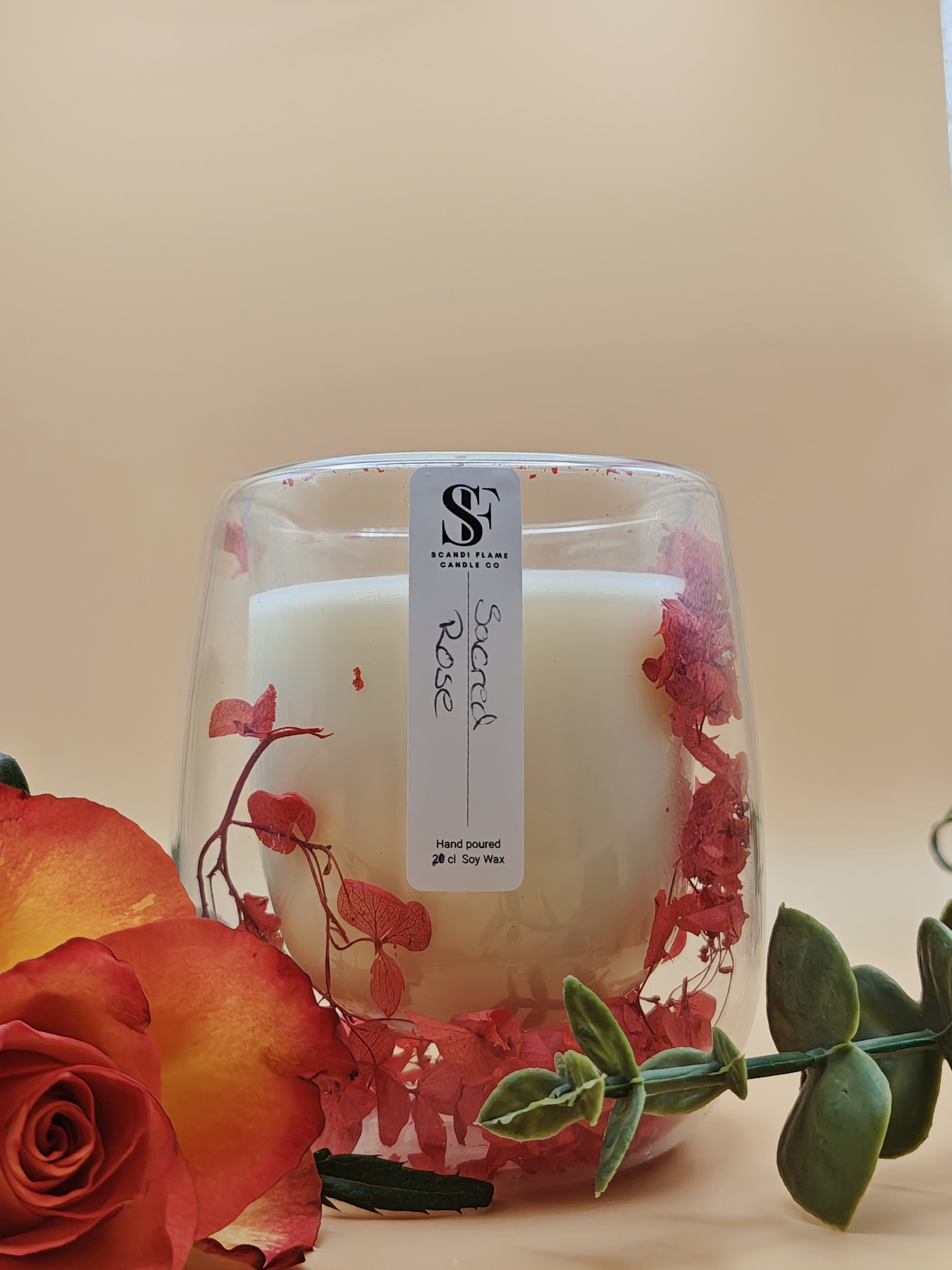 Clear glass jar with red dry flowers in the walls of the jar with 'First Love' label from Scandi Flame with a rose in the foreground