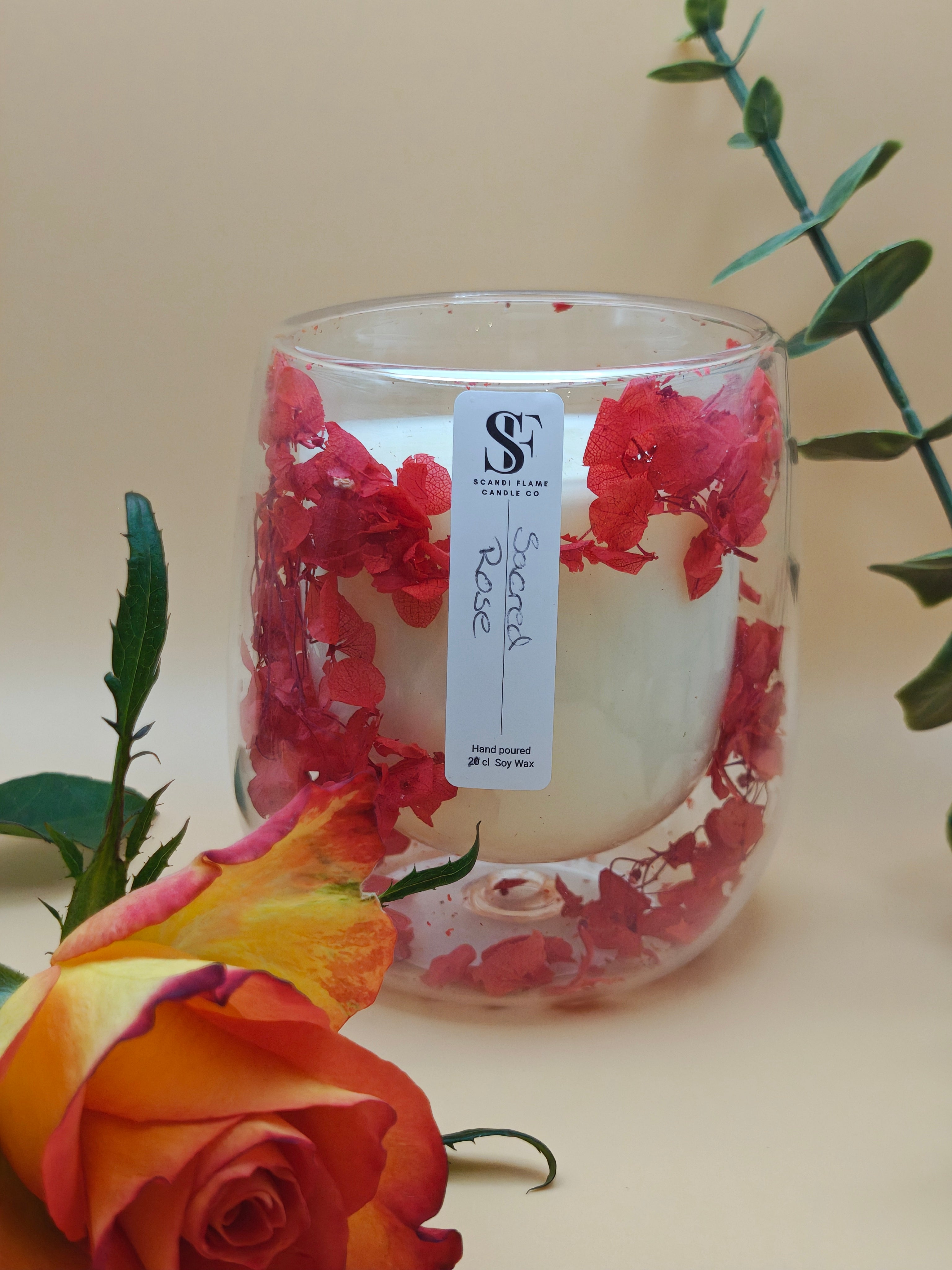 Clear glass jar with red dry flowers in the walls of the jar with 'Sacred Rose' label from Scandi Flame with a rose in the foreground