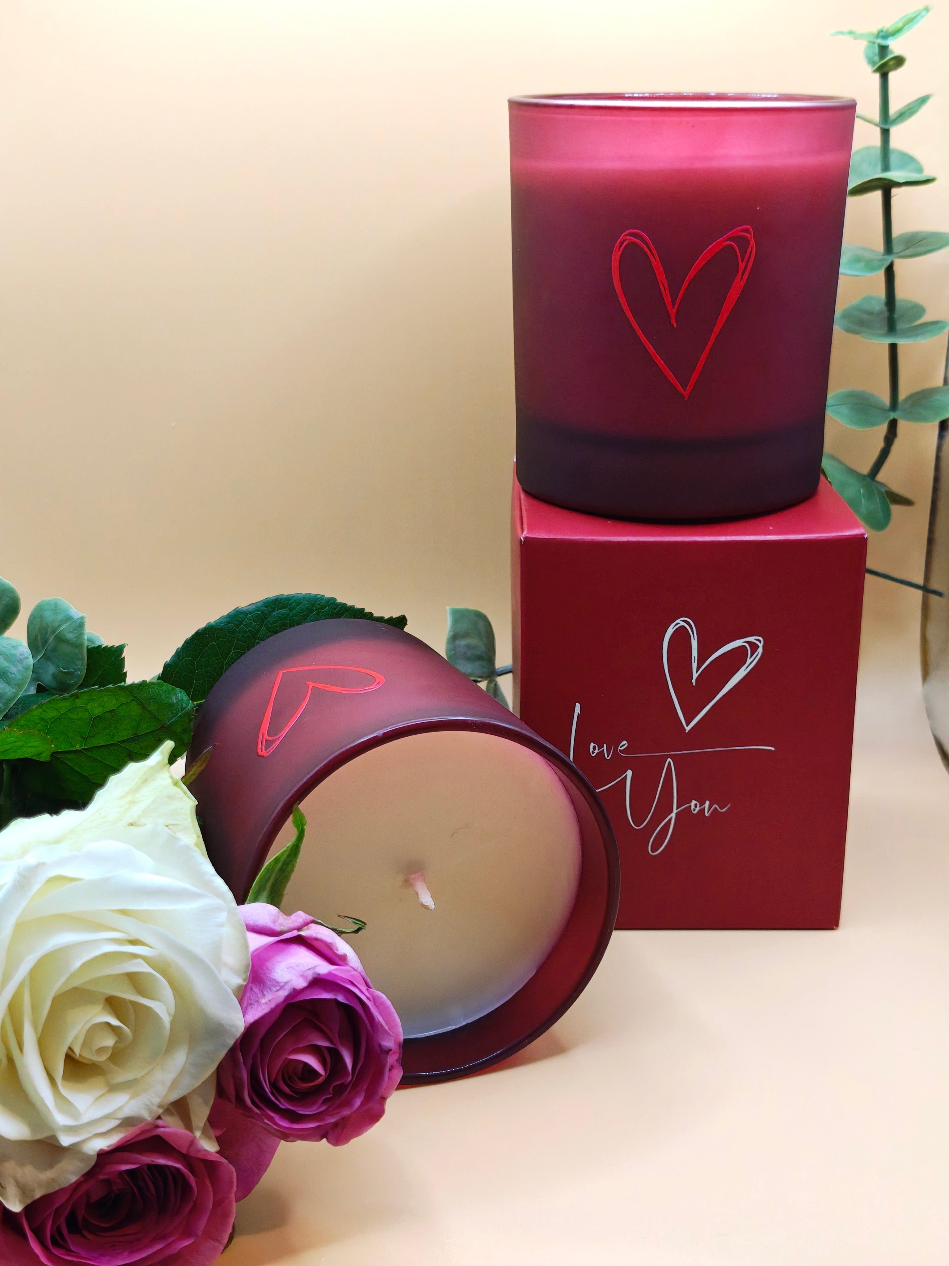 Red candle with a heart design and a decorative box with 'Love you' and flowers on a light background