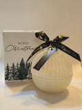 Candle in a round white glass bauble next to a Christmas decorative box with a black ribbon and tag, on a light background